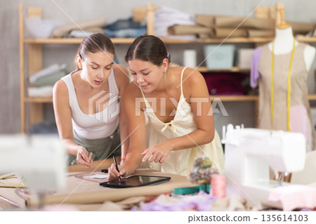 Two female tailor create sketch of dress on tablet Two female tailor create sketch of dress on tablet 135614103