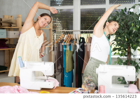 Two young seamstresses doing exercises during break Two young seamstresses doing exercises during break 135614223