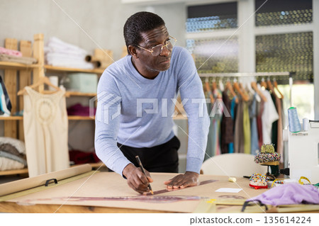 Professional tailor drawing sewing pattern on paper in studio Professional tailor drawing sewing pattern on paper in studio 135614224