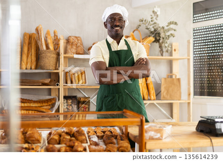 Positive man baker standing at counter in bakehouse Positive man baker standing at counter in bakehouse 135614239