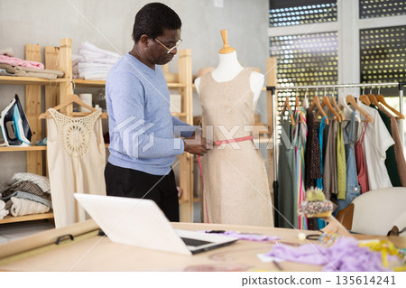 African man seamstress communicates with customer via video call work with mannequin African man seamstress communicates with customer via video call work with mannequin 135614241