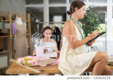 Young female dressmaker drawing on tablet other sew Young female dressmaker drawing on tablet other sew 135614274