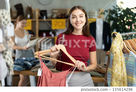 Woman chooses T-shirts against the background of a buyer Woman chooses T-shirts against the background of a buyer 135614296