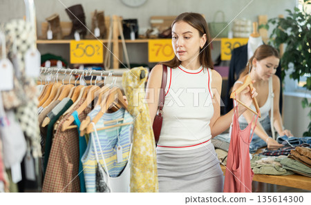 Young girl elect something summer clothing in store. Female client choosing something in background Young girl elect something summer clothing in store. Female client choosing something in background 135614300