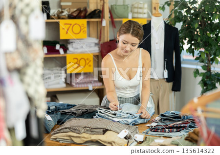 Young woman browsing pants and jeans at outlet store Young woman browsing pants and jeans at outlet store 135614322