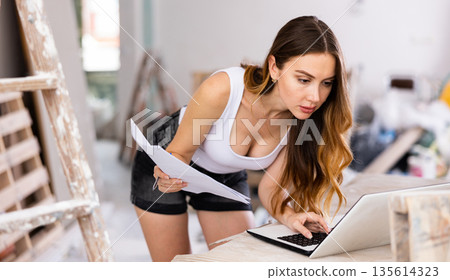 Sexy woman checks the repair plan on a laptop, taking notes on paper Sexy woman checks the repair plan on a laptop, taking notes on paper 135614323