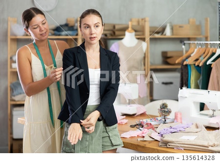woman dressmaker offers a client a sewn jacket in a workshop 135614328