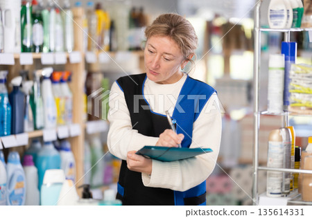 Adult woman seller conducting inventory in store 135614331