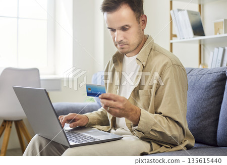Man with laptop and credit card at home, verifying online payment details 135615440