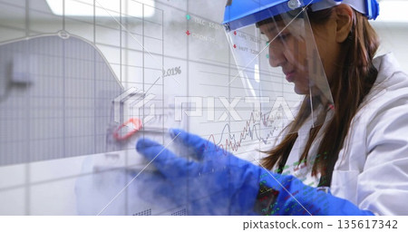 Indian scientist wearing PPE adjusting red clamp on frosted panel in lab with graphs, copy space Indian scientist wearing PPE adjusting red clamp on frosted panel in lab with graphs, copy space 135617342