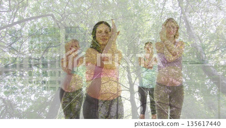 Holding eagle arms pose group practicing yoga at exercise studio, with yoga mats and forest overlay Holding eagle arms pose group practicing yoga at exercise studio, with yoga mats and forest overlay 135617440