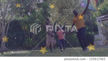Running family of three holding hands across backyard lawn with colorful kite and golden stars 135617465