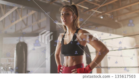 Training boxer wearing black sports bra, red hand wraps in ring with punching bag, digital overlay 135617503