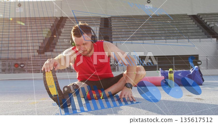Stretching male athlete wearing headphones, smartwatch on running track, with prosthetic blade 135617512