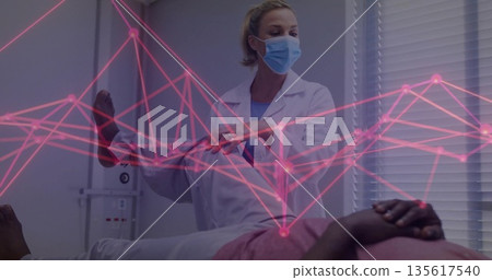 Masked doctor in lab coat lifting and inspecting patient's leg in clinic, with pink network overlay 135617540