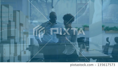 Examining tablet two colleagues standing by desk in open-plan office, with storage cabinets 135617573