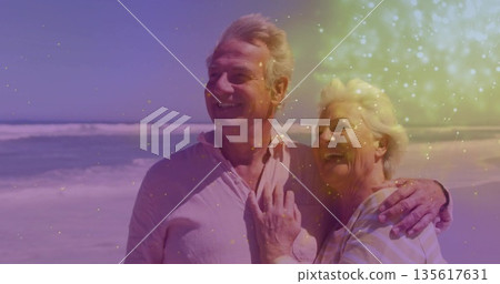 Smiling senior couple standing on sandy shore, wearing button-up shirt, striped top, clear sky Smiling senior couple standing on sandy shore, wearing button-up shirt, striped top, clear sky 135617631