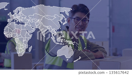 Smiling Korean man wearing safety vest leaning on box stack in warehouse, with world map overlay Smiling Korean man wearing safety vest leaning on box stack in warehouse, with world map overlay 135617642