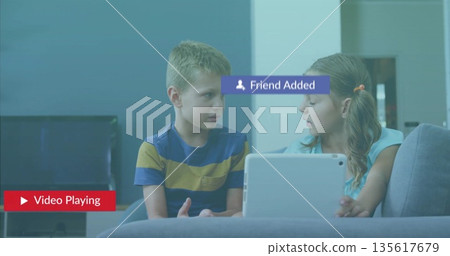 Watching two children sharing white tablet on gray couch in living room, with playback icon 135617679