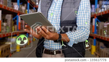 Business casual supervisor monitoring tablet in warehouse aisle with boxes, floating energy icons 135617778