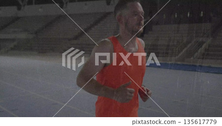 Jogging runner wearing orange shirt and dark shorts on stadium track with empty seating, copy space 135617779