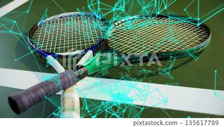 Pair of tennis rackets lying crossed over boundary line on court, with neon teal network overlay 135617789