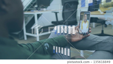 Holding smartphone, African American man conducting call in office, with holographic charts 135618849