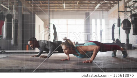 Performing push-ups workout partners wearing sportswear on rubber mat in gym, with punching bags 135618870
