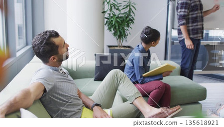 Collaborating four office colleagues sitting on green sofa in meeting area, using yellow folder Collaborating four office colleagues sitting on green sofa in meeting area, using yellow folder 135618921