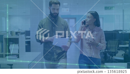 Walking colleagues reviewing document while speaking on smartphone in office corridor, data overlay Walking colleagues reviewing document while speaking on smartphone in office corridor, data overlay 135618925