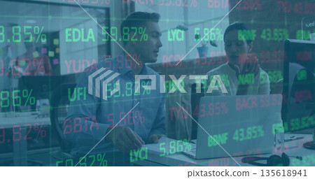 Coworkers wearing shirt and blouse discussing stock data on laptop with tickers in open office Coworkers wearing shirt and blouse discussing stock data on laptop with tickers in open office 135618941