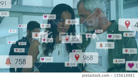 Four marketing professionals collaborating on tablet analyzing social media icons in modern office 135618981