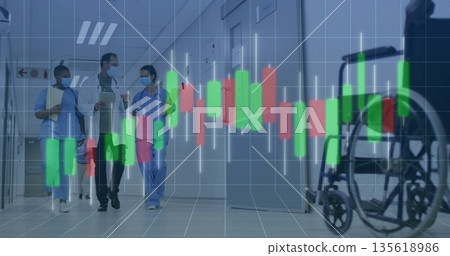 Walking masked team wearing scrubs and coat discussing patient info in corridor, with wheelchair 135618986