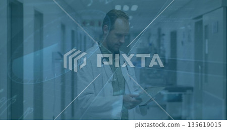 Reading clipboard male doctor standing hospital corridor under lights, holding stethoscope by cart 135619015