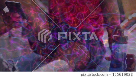 Sitting man wearing red top holding smartphone and blue vape device on couch, neon light trails 135619028