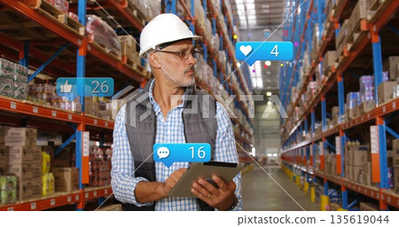 Inspecting worker in safety gear recording inventory on tablet in warehouse, with reaction icons Inspecting worker in safety gear recording inventory on tablet in warehouse, with reaction icons 135619044