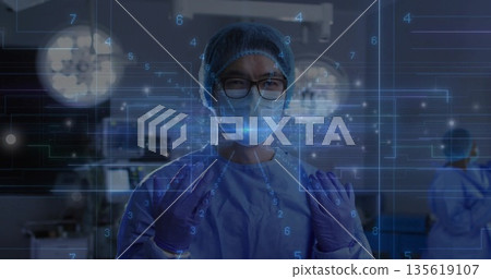Standing Chinese surgeon wearing scrubs, gloves and mask in operating room, with digital overlays Standing Chinese surgeon wearing scrubs, gloves and mask in operating room, with digital overlays 135619107