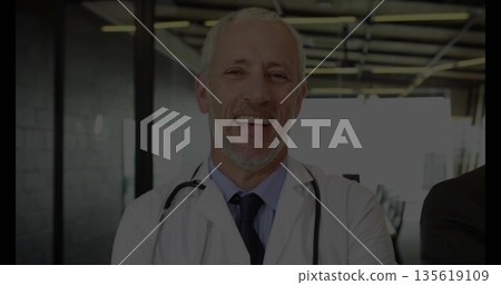Smiling senior male doctor standing in modern clinic lobby, with stethoscope and white lab coat Smiling senior male doctor standing in modern clinic lobby, with stethoscope and white lab coat 135619109
