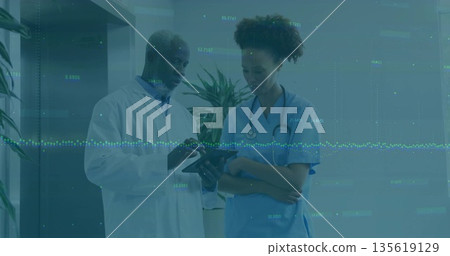 Pointing physician showing data on tablet to nurse in hospital corridor, with stethoscope 135619129