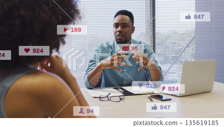 Gesturing man in teal shirt discussing media analytics in conference room, with laptop 135619185