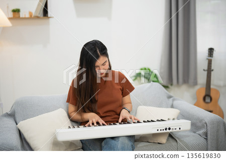 Young woman playing keyboard at home, enjoying music in a cozy living room with natural light and comfortable furniture, creative hobby and relaxation 135619830
