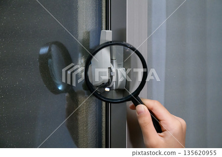Image of a security guard inspecting a window lock with a magnifying glass Image of a security guard inspecting a window lock with a magnifying glass 135620955