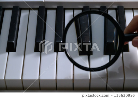 Examining piano keys with a magnifying glass Examining piano keys with a magnifying glass 135620956