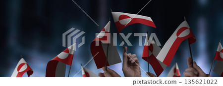 Greenland flags in their hands on a blurred urban background Greenland flags in their hands on a blurred urban background 135621022