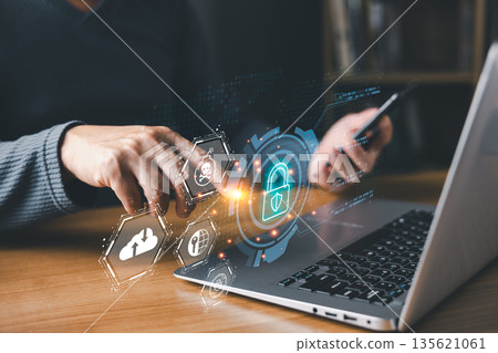 person using a laptop and smartphone interacts with glowing digital icons of a lock, shield, and skull, symbolizing cybersecurity, online protection, data security, and defense against cyber threats. 135621061