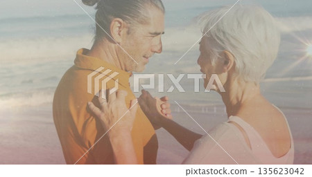 Couple in orange polo and white top holding hands in waves at beach, showing wedding ring 135623042