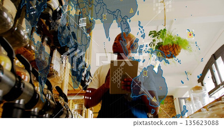 Barista holding tablet and consulting map overlay at coffee counter, wearing dark apron over shirt Barista holding tablet and consulting map overlay at coffee counter, wearing dark apron over shirt 135623088