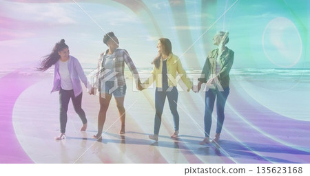 Walking four friends in jackets holding hands along beach at low tide, with sunlight lens flare Walking four friends in jackets holding hands along beach at low tide, with sunlight lens flare 135623168