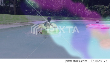 Floating siblings wearing swimsuit and trunks in backyard pool, with green, yellow inflatable rings 135623173