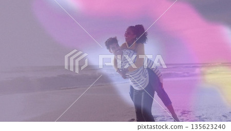 Giving piggyback ride couple in casual wear at shoreline with lapping ocean waves, pastel flares Giving piggyback ride couple in casual wear at shoreline with lapping ocean waves, pastel flares 135623240